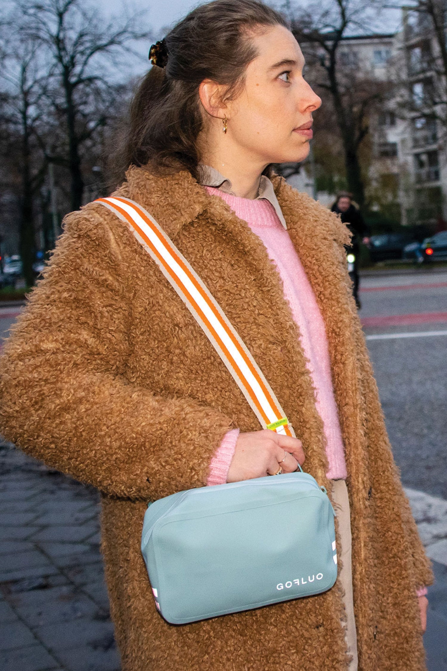 Woman wearing a brown coat with a light blue bag on a street.