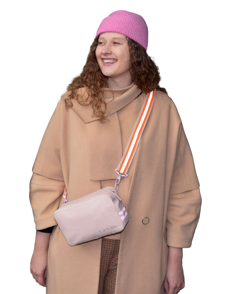 Person wearing a beige coat and pink beanie with a beige crossbody bag on a white background