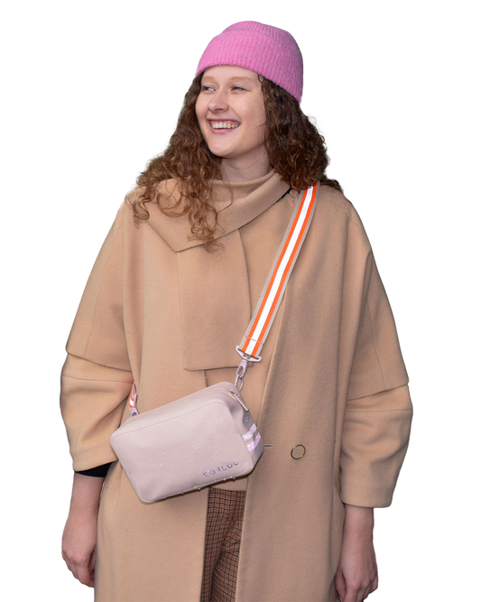 Person wearing a beige coat and pink beanie with a beige crossbody bag on a white background