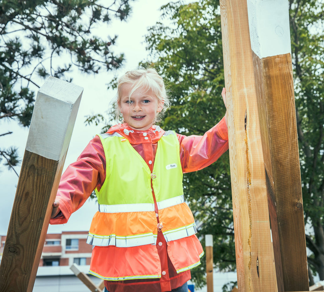 Child in a safety vest standing outdoors with wooden planks