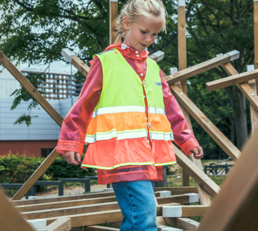 Child wearing a high-visibility safety vest on a wooden structure