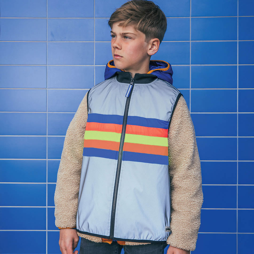 Child wearing a colorful striped jacket against a blue tiled wall