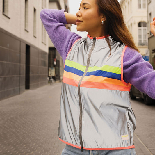 Woman wearing a gray jacket with rainbow stripes on a city street
