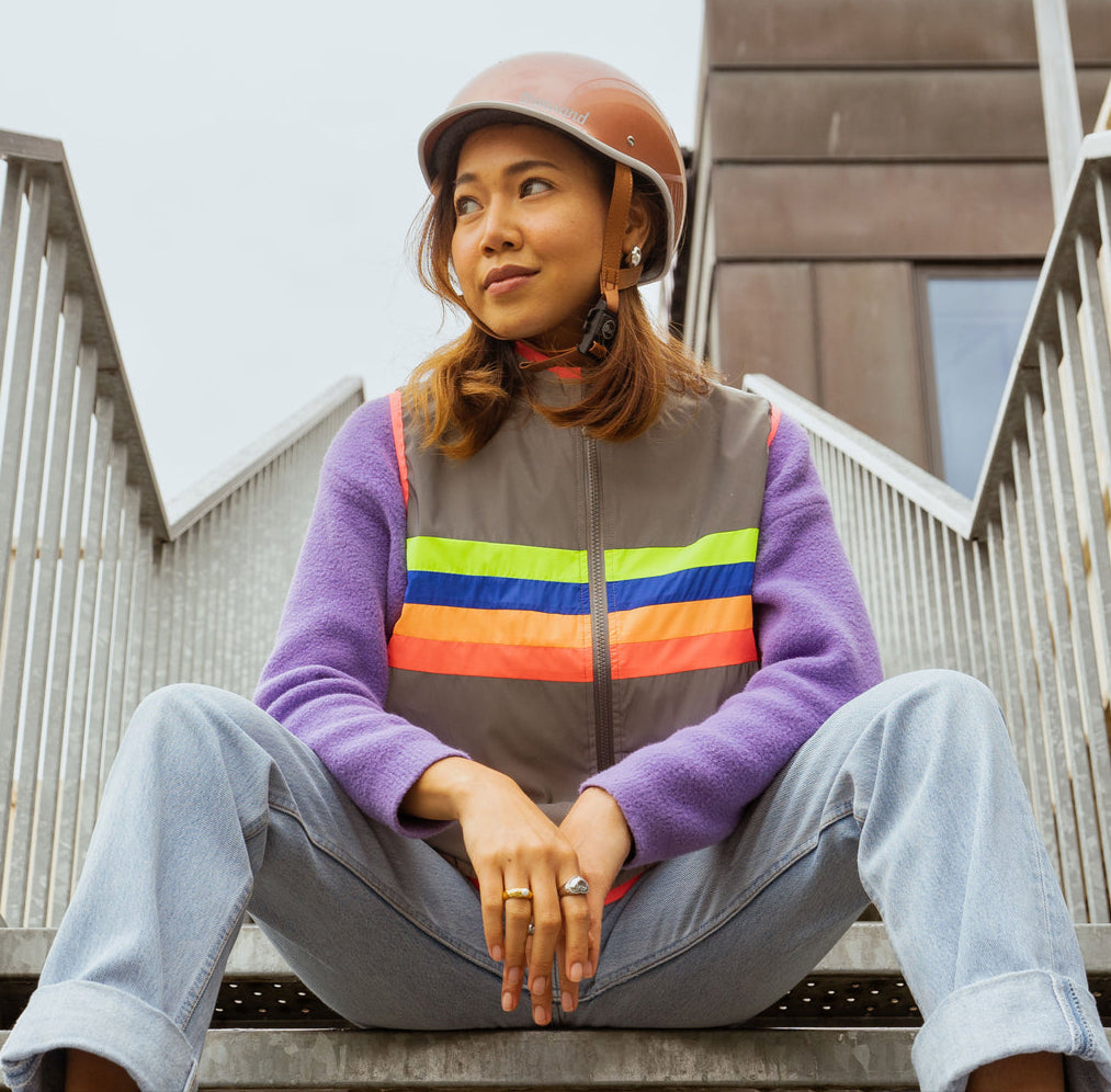 Person sitting on steps wearing a colorful vest and helmet.