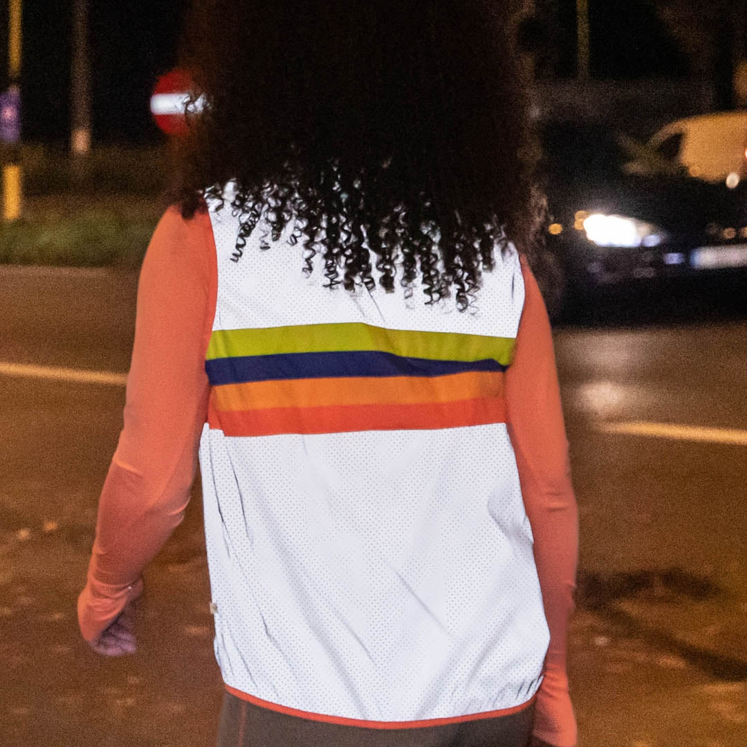 Person wearing a white vest with colorful stripes on a street at night.