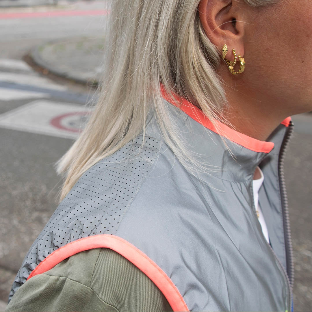 Person wearing a grey and green jacket with pink accents, standing on a street.