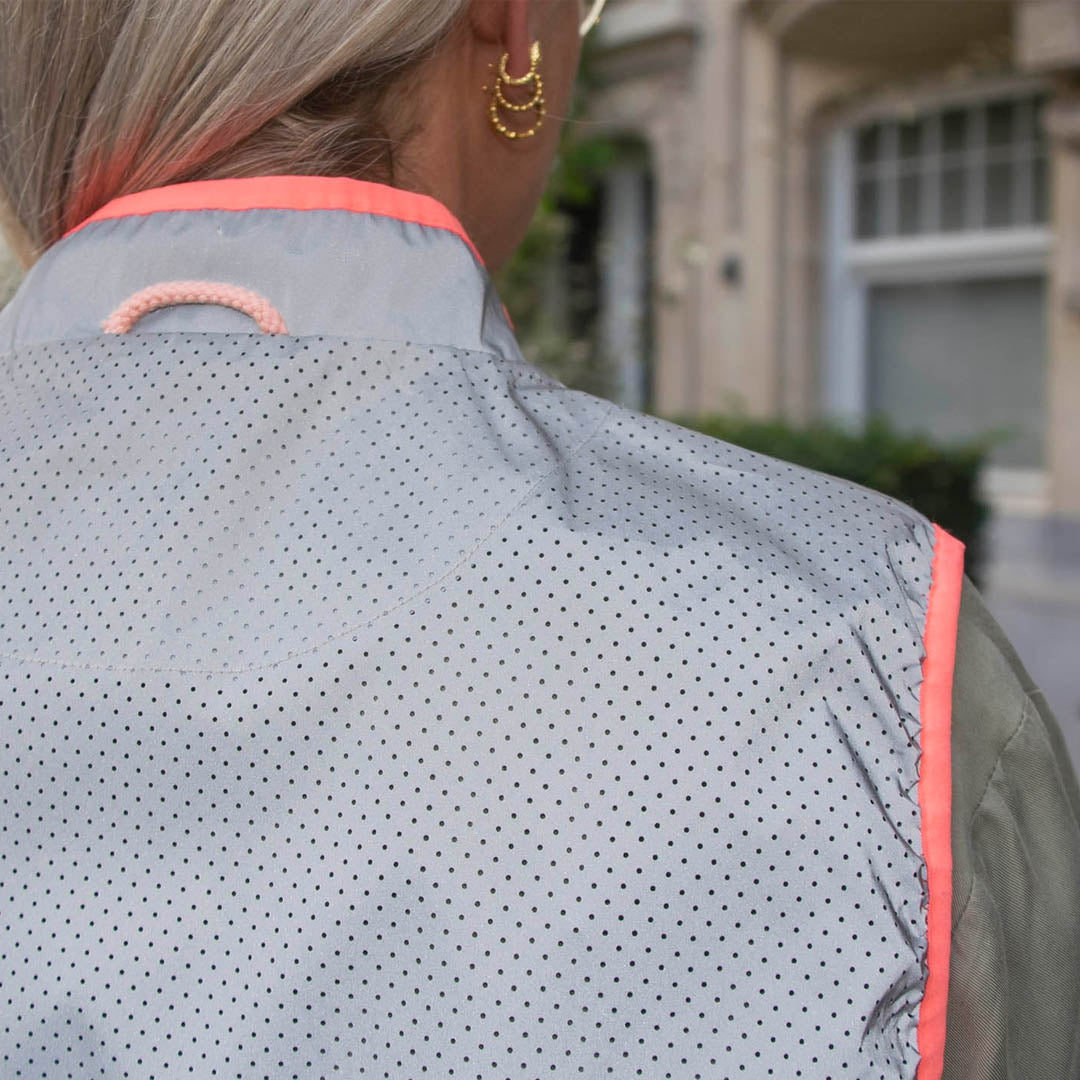Person wearing a light gray jacket with pink trim, standing outdoors.