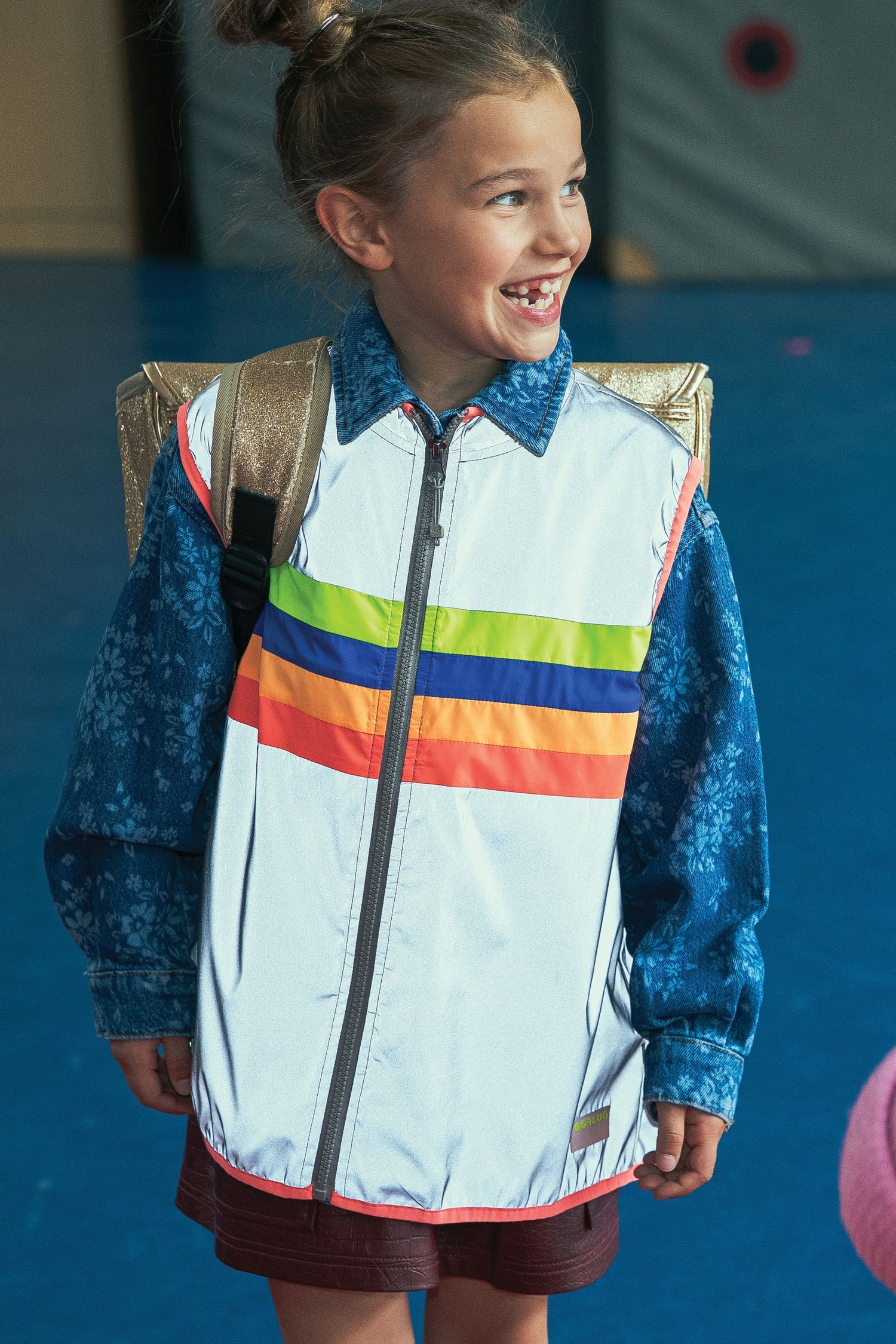 Young girl wearing a colorful jacket with a rainbow design against a blue background