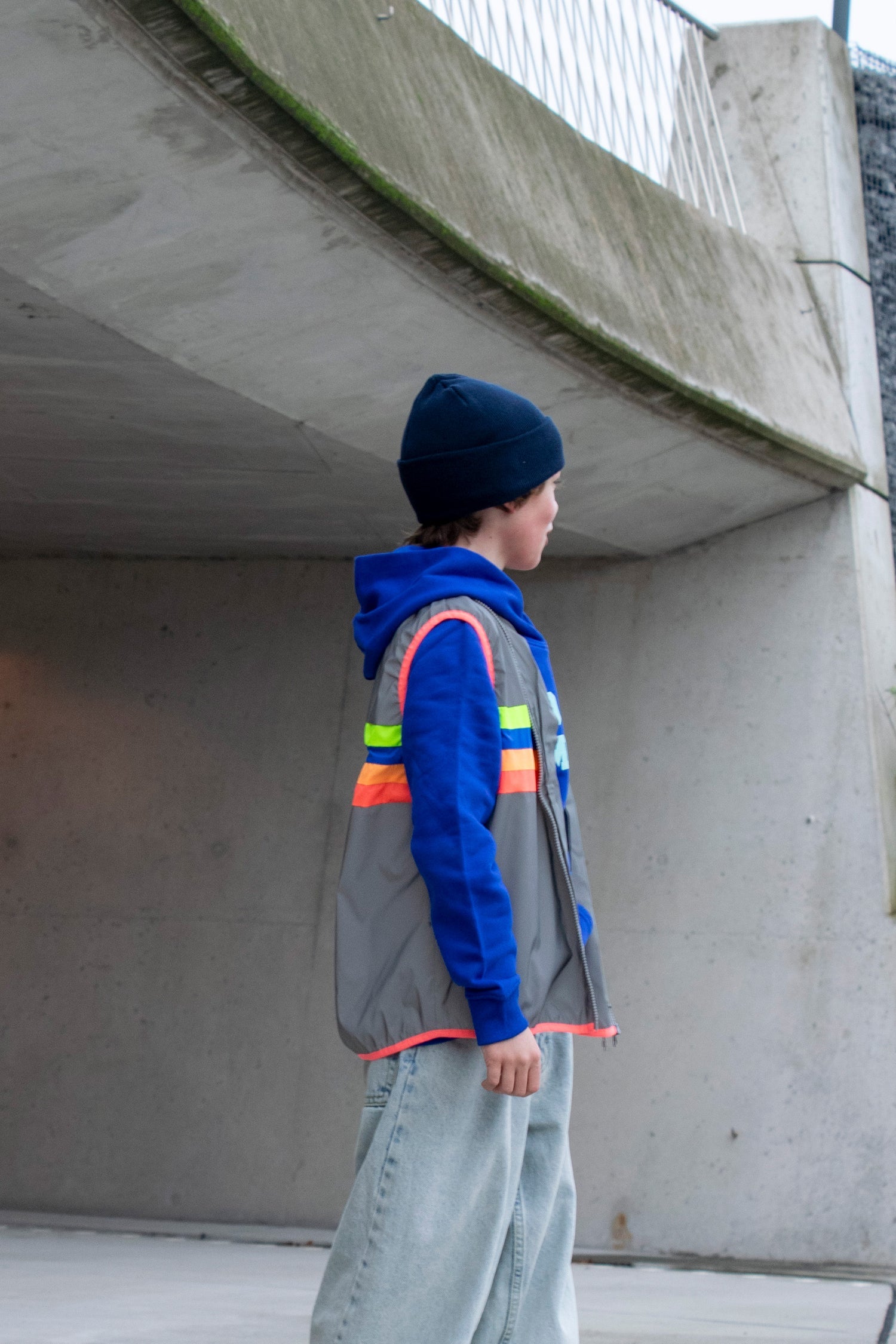 Person wearing a reflective vest and blue hoodie standing under a concrete overpass.