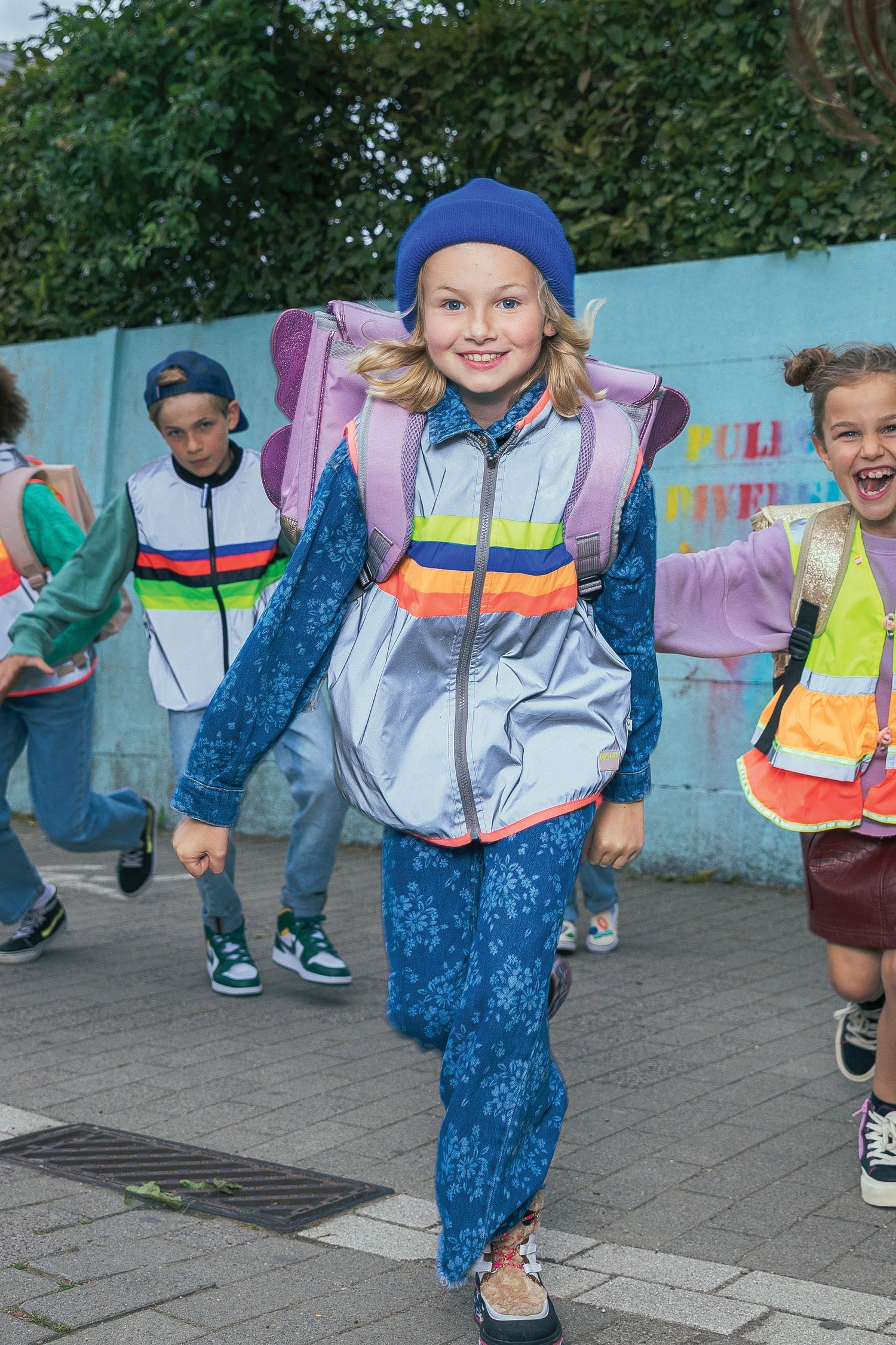 Children in colorful outfits running on a sidewalk with a mural in the background