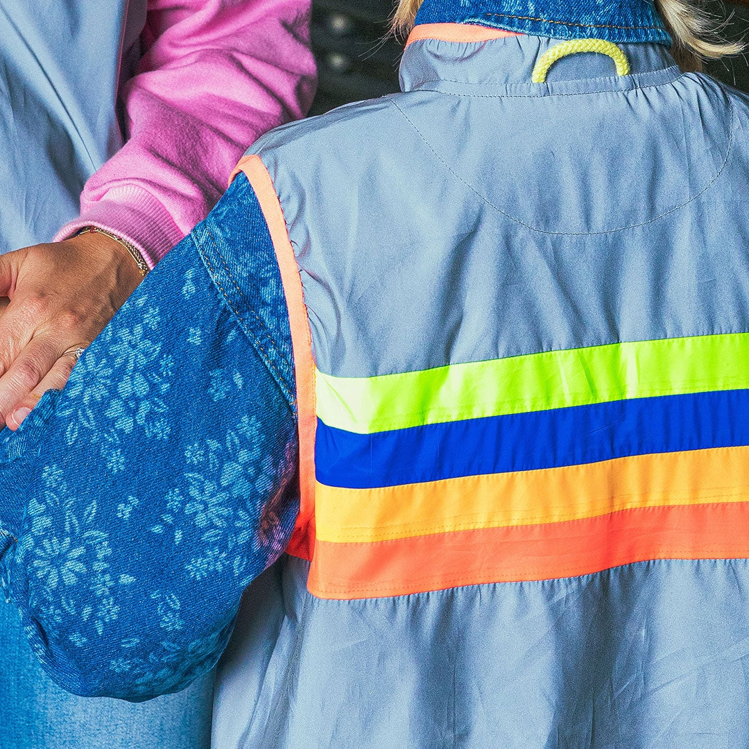 Person wearing a blue jacket with rainbow stripes, holding hands with another person.