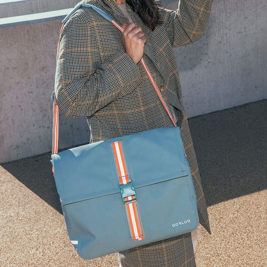 Person carrying a blue bag with orange accents against a concrete wall.