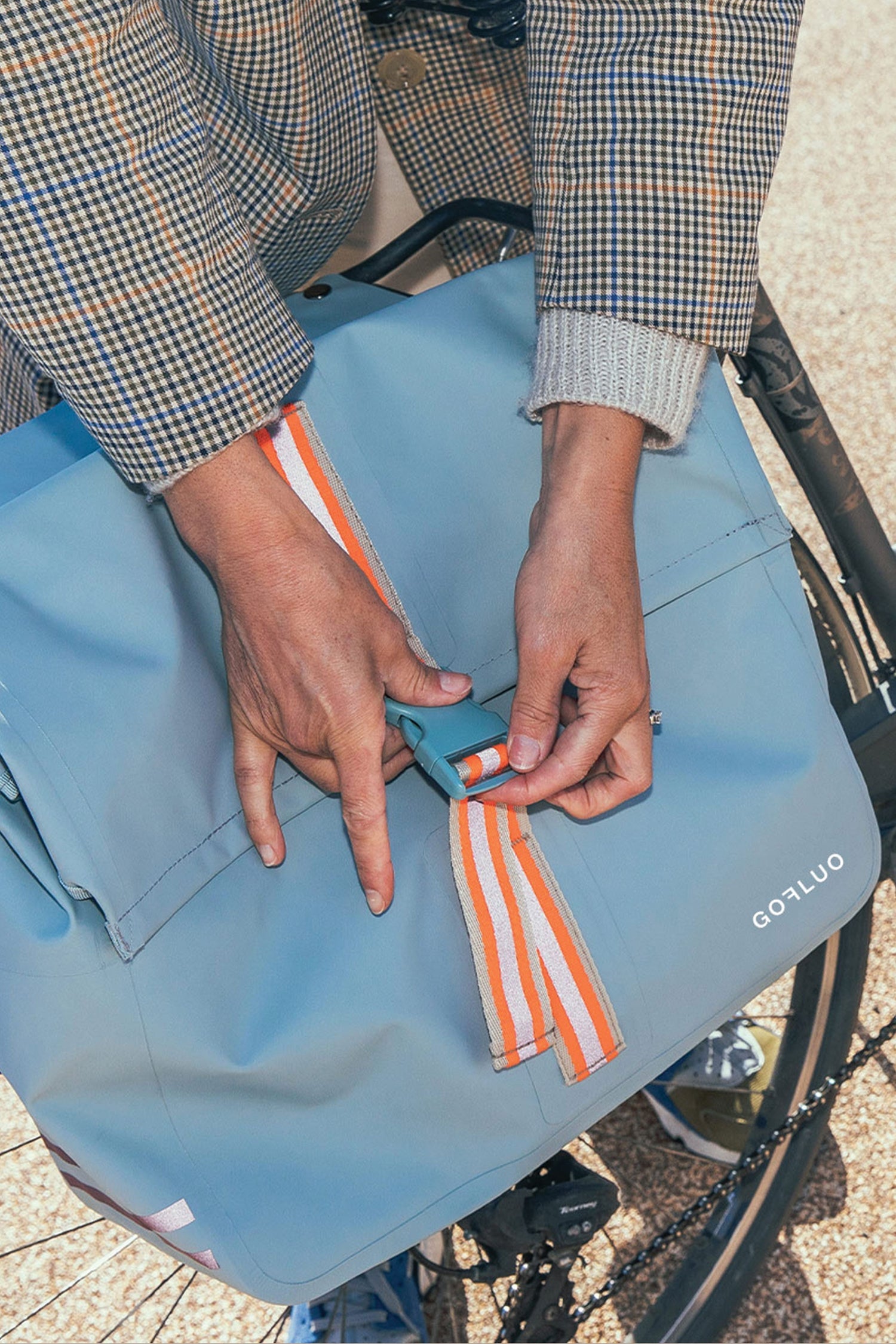 Person adjusting a blue bag with orange straps on a bicycle.
