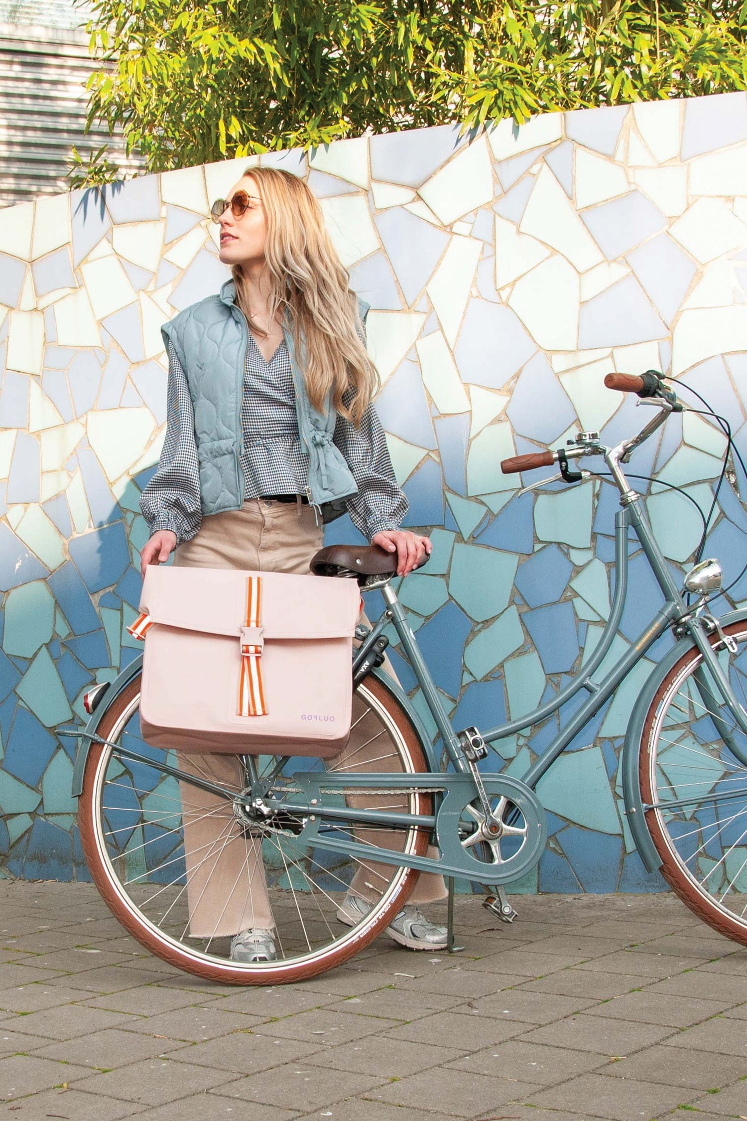 Woman with a bicycle and pink bag against a mosaic wall