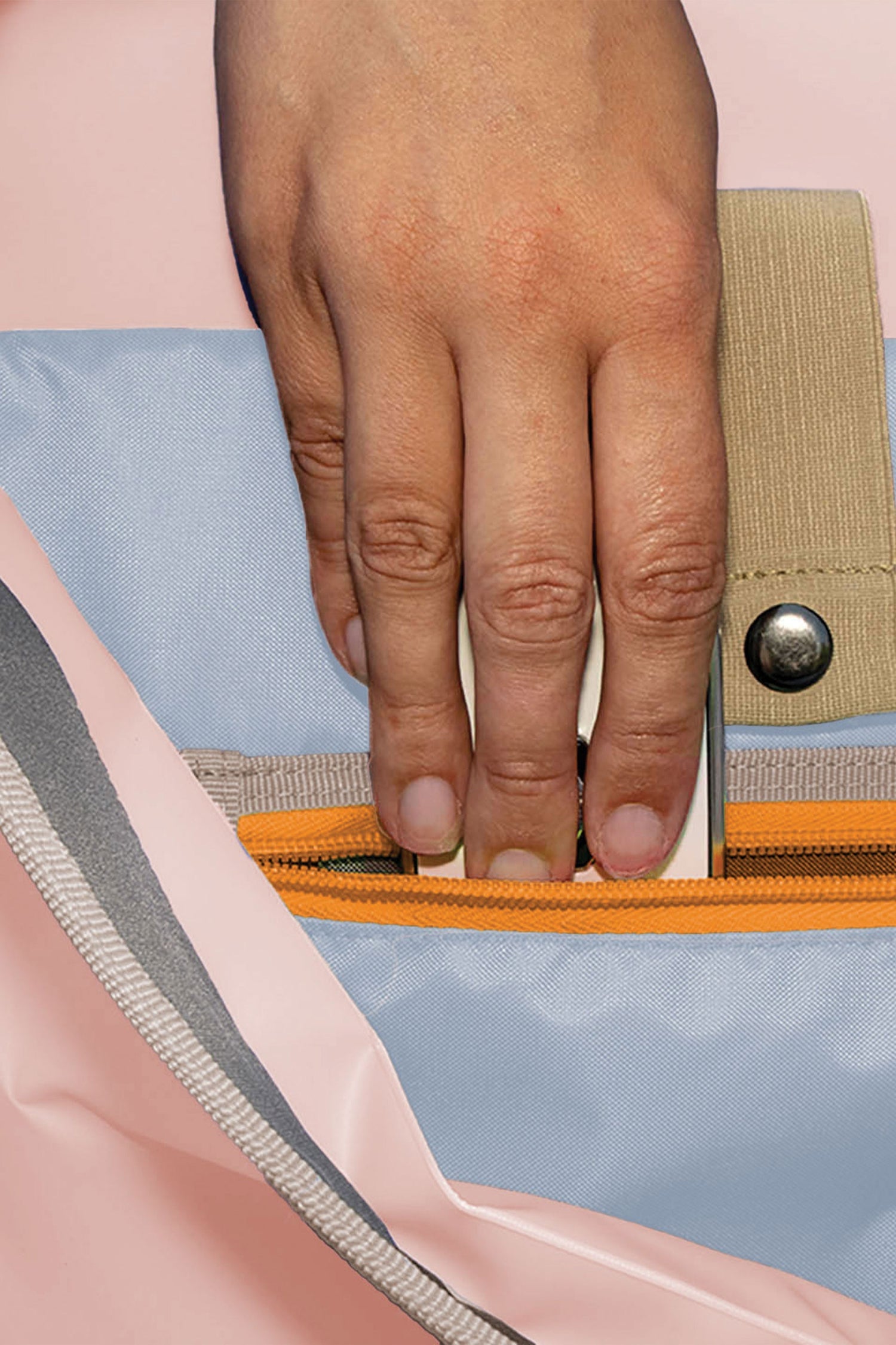 Close-up of a hand zipping a colorful bag with a pink, blue, and beige design.