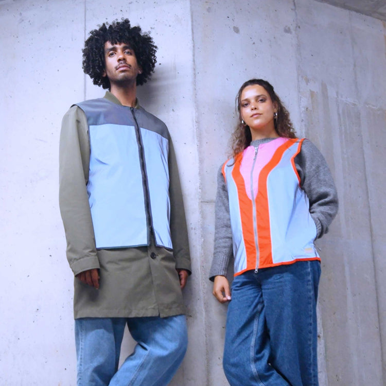 Two people wearing colorful hi-vis clothing against a concrete wall.