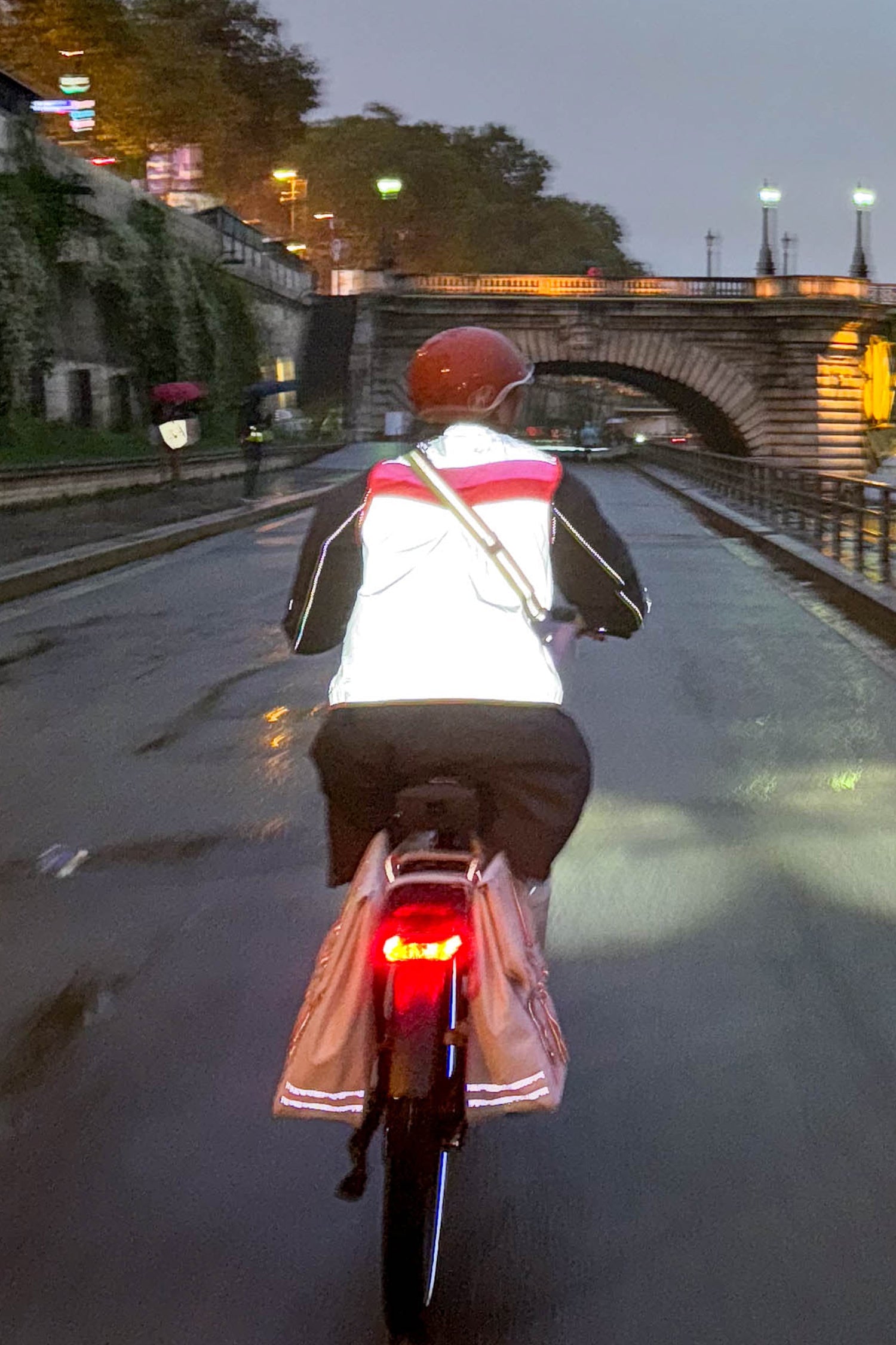 Person riding a bicycle on a wet street with reflective gear and a helmet.