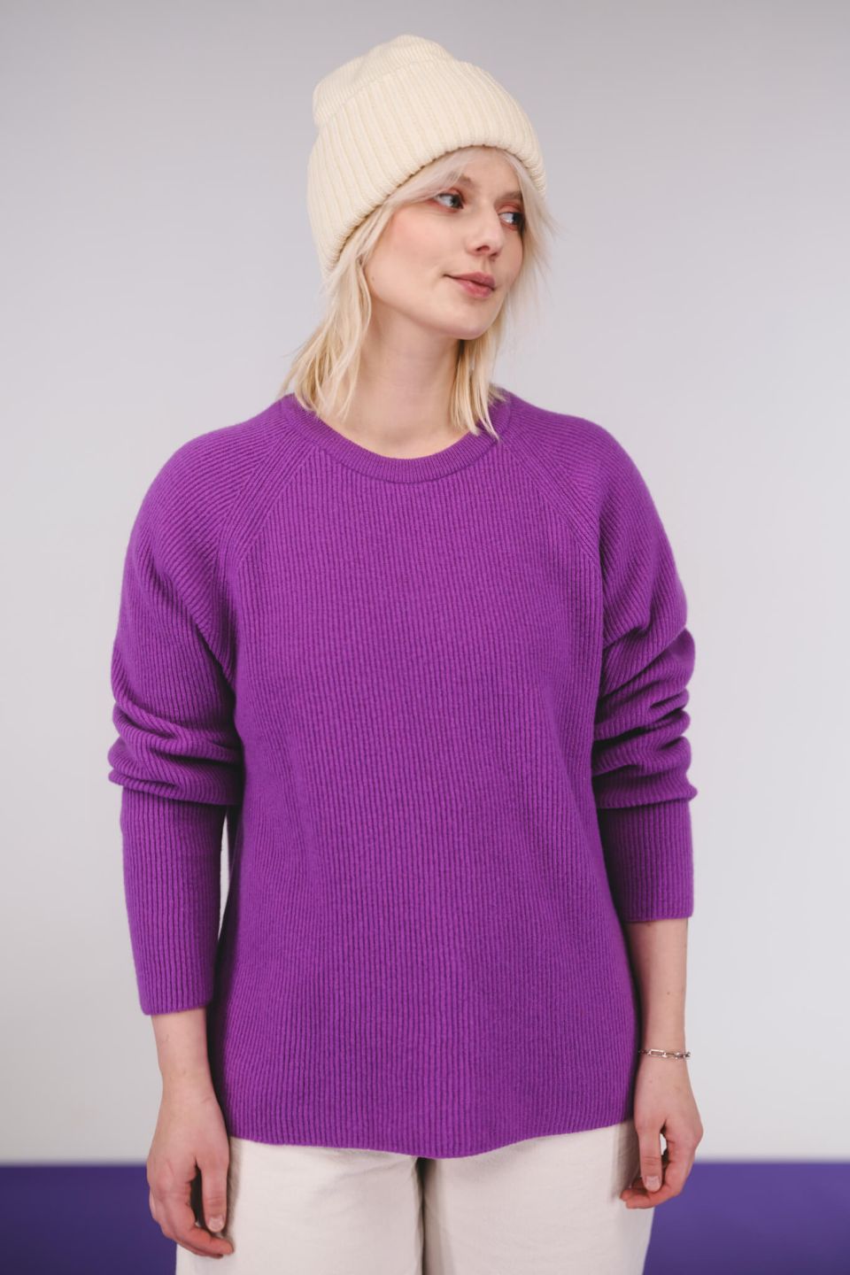 Person wearing a purple sweater and cream beanie against a plain background