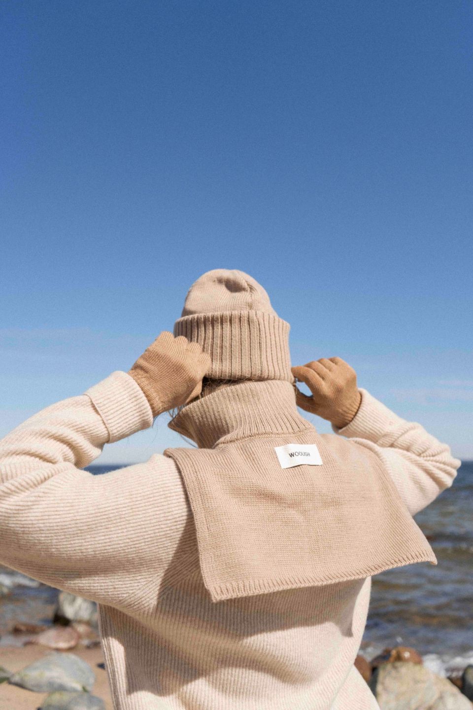 Person wearing a beige knit sweater and hat by the beach