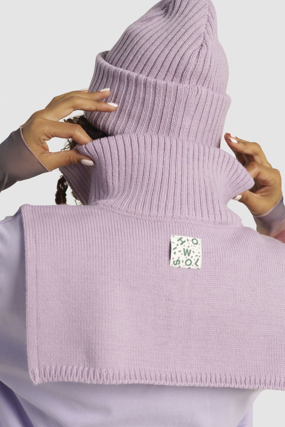 Person wearing a light purple ribbed sweater with a brand logo on a white background