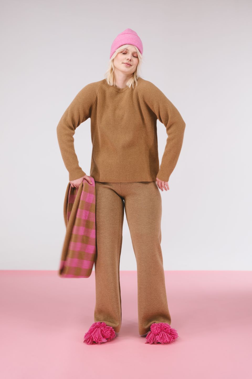 Person wearing a brown outfit with pink accents on a pink platform against a white background