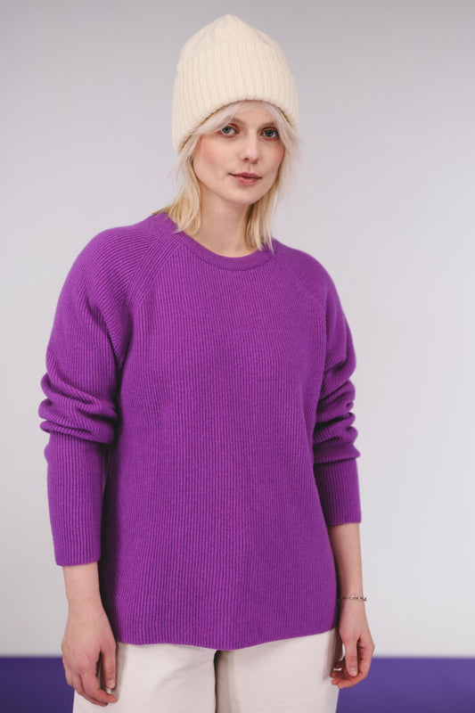 Person wearing a purple sweater and cream beanie against a white background
