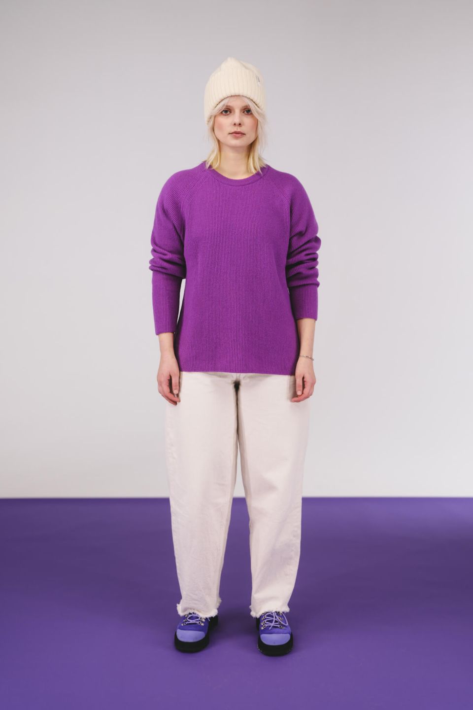 Person wearing a purple sweater and white pants on a purple and white background