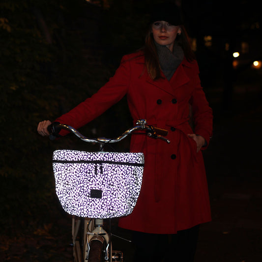 Person wearing a red coat with an illuminated bicycle basket at night.